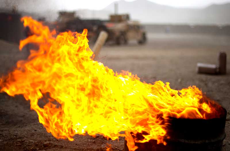 fire burns in foreground military vehicles in background