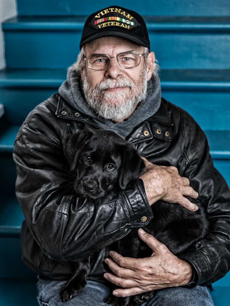 Veteran holds black puppy during VA service dog training.